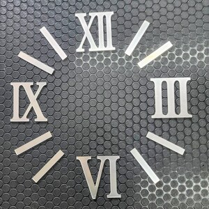 以下が含まれることがあります： ローマ数字の文字盤要素、XII、III、VI、IXの数字と、対応する時間マーカー。暗いグレーのテクスチャ加工された表面に配置されています。