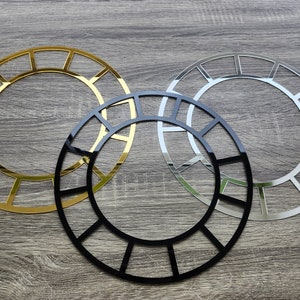 Könnte beinhalten: Drei dekorative Wanduhrenrahmen in Gold, Silber und Schwarz. Jeder Rahmen ist rund mit einem geometrischen Muster aus Quadraten.