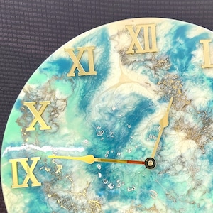 May include: A blue and white resin clock face with gold Roman numerals and gold hands. The clock face has a marbled, abstract design.