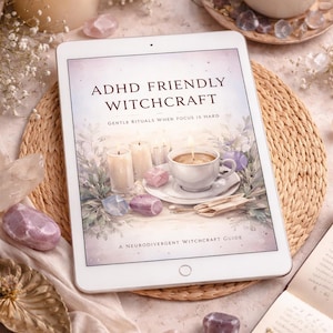 May include: A tablet displays the book cover for "ADHD Friendly Witchcraft." The image includes a lit candle, a cup of tea, crystals, and a book. The text on the cover reads "Gentle Rituals When Focus Is Hard" and "A Neurodivergent Witchcraft Guide."
