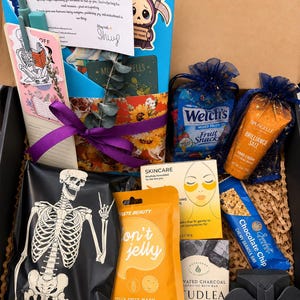 May include: A gift box containing a skeleton-printed pouch, a pineapple jelly sheet mask, a chocolate chip granola bar, a charcoal cleansing bar, a Spongelle hand cream, Welch's fruit snacks, a skincare eye mask, a pen, and a thank you note.