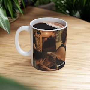 May include: White ceramic coffee mug with a collage of romantic images. The mug is filled with dark liquid, likely coffee. The handle is white, and the mug sits on a wooden surface.