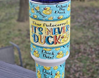 May include: A white tumbler with a blue and yellow design featuring rubber ducks and the text "Dear Autocorrect It's Never Duck This!"  What The Duck! Duck This!  Duck It All!"