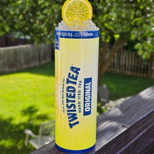 May include: A yellow can of Twisted Tea Hard Iced Tea with a lemon wedge on top. The can has blue text that reads "Made with Real Brewed Tea" and "Twisted Tea Hard Iced Tea Original".