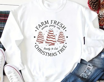 May include: White sweatshirt with a black and red graphic of three Christmas trees that look like cake. The text reads "Farm Fresh Sprinkles Frosting Cake Ready to Eat Christmas Tree".