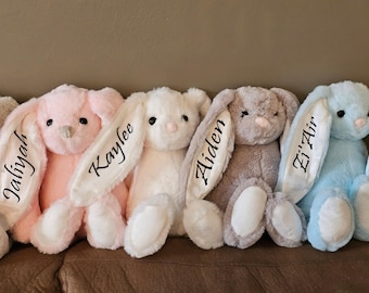 May include: Five plush bunny rabbits with embroidered names on their ears. The bunnies are pink, white, gray, light blue, and a darker shade of blue.