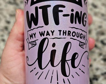 May include: A light purple tumbler with the text "I'M JUST WTF-ING MY WAY THROUGH life" in black script. The tumbler has a pearlescent finish and is held by a hand.