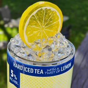 May include: A blue and yellow can with the text "Hard Iced Tea with a Twist of Lemon" and "5% Alc./Vol."  The can is topped with ice and a yellow lemon slice.