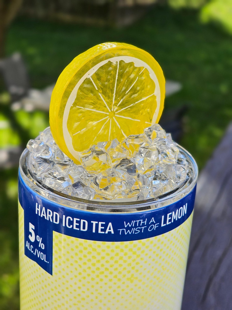 May include: A blue and yellow can with the text "Hard Iced Tea with a Twist of Lemon" and "5% Alc./Vol."  The can is topped with ice and a yellow lemon slice.