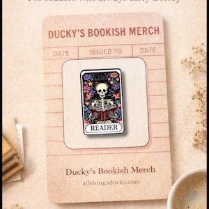 May include: Bookish enamel pin featuring a skeleton reading a book, surrounded by colorful flowers. The pin is on a card that says "Ducky's Bookish Merch" and "Reader". The image also includes a cup of coffee and the text "For readers who always carry a story".