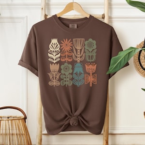 May include: A brown t-shirt with a graphic print of colorful stylized flowers. The flowers are in a grid pattern and are outlined in black.