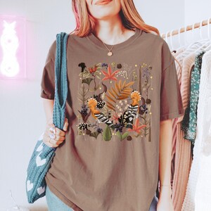 May include: A brown t-shirt with a colorful illustration of two birds in a floral pattern.