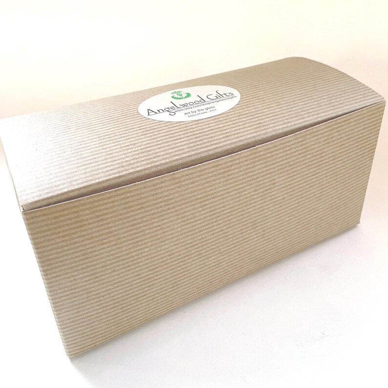May include: A rectangular, corrugated cardboard gift box with a curved lid. The box is light brown and has a textured surface. A white oval sticker with green text that reads "Angelwood Gifts" is on the lid.