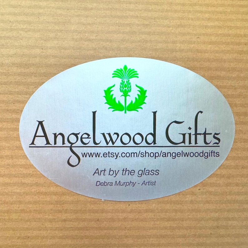 May include: Oval silver sticker with the text "Angelwood Gifts" in black, a green thistle emblem, and the website address www.etsy.com/shop/angelwoodgifts. The text "Art by the glass" and artist's name "Debra Murphy" are also included.