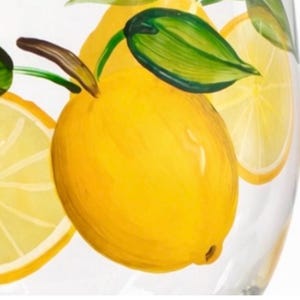 May include: Clear glass with a hand-painted lemon design. The lemons are yellow with green leaves and brown stems. Slices of lemon are also painted on the glass. The design is a bright and cheerful addition to any kitchen.