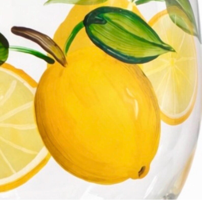 May include: Clear glass with a hand-painted lemon design. The lemons are yellow with green leaves and brown stems. Slices of lemon are also painted on the glass. The design is a bright and cheerful addition to any kitchen.