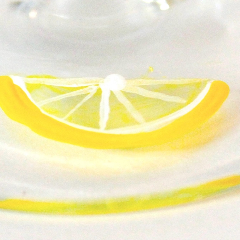 May include: A close-up of a painted lemon slice with a white interior and a bright yellow rind. The lemon slice is set against a soft, white background, creating a fresh and vibrant aesthetic. The image evokes a sense of refreshment and citrus.