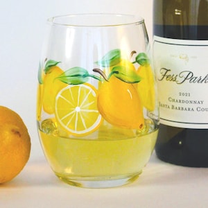 lemons and green leaves. A bottle of Chardonnay wine is partially visible in the background. The glass is on a white surface.