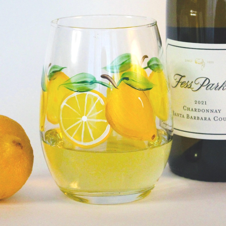 lemons and green leaves. A bottle of Chardonnay wine is partially visible in the background. The glass is on a white surface.