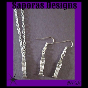 May include: Silver-toned Big Ben jewelry set, including a necklace and a pair of earrings. The necklace features a chain with a Big Ben pendant, and the earrings have a hook design. The image includes the text "Saporas Designs" and the number "#458".