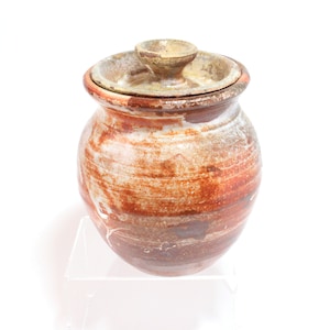 May include: A brown and white ceramic jar with a lid. The jar has a rustic, handmade look and is decorated with streaks of brown and white glaze.