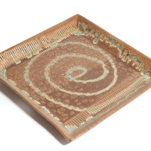 May include: A square ceramic serving tray with a brown glaze and a white spiral design. The tray has a textured border.