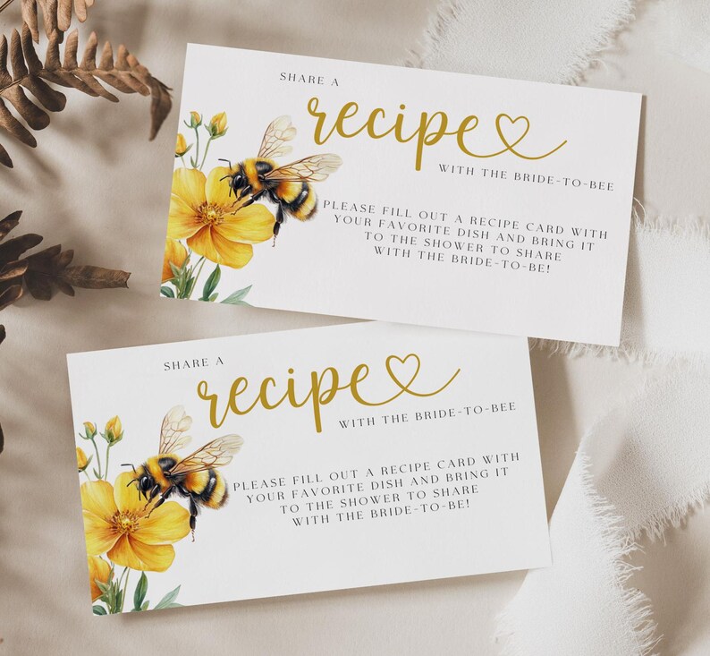 K&ouml;nnte beinhalten: Zwei wei&szlig;e Karten mit goldener Schrift, auf denen "Teile ein Rezept mit der Braut zu sein" steht. Die Karten zeigen eine Biene und gelbe Blumen.