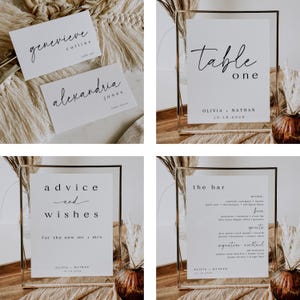 May include: A selection of wedding stationery, featuring place cards and framed signs. The place cards show names such as "Genevieve" and "Alexandria." The signs display "Table One," "Advice and Wishes," and "The Bar," with names and a date.