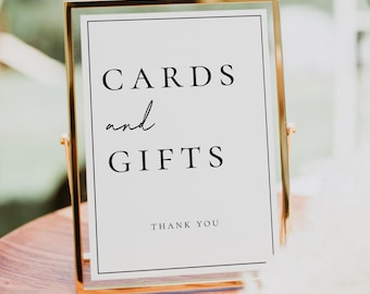 May include: A gold-framed sign with a white background and black text that reads "CARDS and GIFTS THANK YOU".