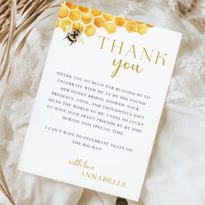 K&ouml;nnte beinhalten: Eine Dankeskarte mit einer Aquarell-Illustration eines Bienenstocks und einer Biene. Der Text lautet "Danke" in goldenen Buchstaben und enth&auml;lt eine Nachricht, die sich bei den G&auml;sten f&uuml;r die Teilnahme an einer Bridal Shower bedankt. Die Karte ist mit "mit Liebe, Annabelle" signiert.