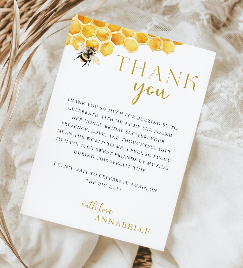 K&ouml;nnte beinhalten: Eine Dankeskarte mit einer Aquarell-Illustration eines Bienenstocks und einer Biene. Der Text lautet "Danke" in goldenen Buchstaben und enth&auml;lt eine Nachricht, die sich bei den G&auml;sten f&uuml;r die Teilnahme an einer Bridal Shower bedankt. Die Karte ist mit "mit Liebe, Annabelle" signiert.