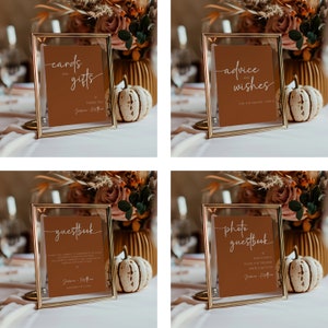 May include: Four gold-framed signs with brown cardstock inserts. The signs are labeled "cards and gifts", "advice and wishes", "guestbook", and "photo guestbook". Each sign has a handwritten font and the text "JM" at the bottom.