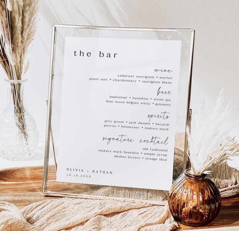 May include: A clear framed sign with the words "the bar" at the top. The sign lists wine, beer, spirits, and signature cocktail options. The names Olivia and Nathan are at the bottom, with the date 10.16.2025.