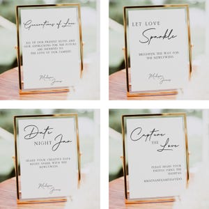 May include: Four gold-framed signs with white backgrounds and black text. The signs are for a wedding and include the text "Generations of Love", "Let Love Sparkle", "Date Night Jar", and "Capture the Love".