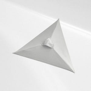 May include: A white fabric pyramid-shaped object with smooth, taut surfaces meeting at a central apex. The structure features clean, straight edges and a small, gathered fabric detail at the top point, creating a geometric and symmetrical form.
