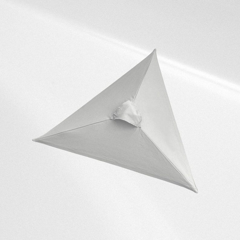 May include: A white fabric pyramid-shaped object with smooth, taut surfaces meeting at a central apex. The structure features clean, straight edges and a small, gathered fabric detail at the top point, creating a geometric and symmetrical form.