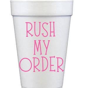 May include: A white foam cup with the words "RUSH MY ORDER" in pink lettering. The cup is cylindrical with a slightly flared top and is set against a plain white background.