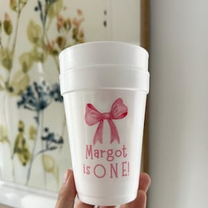 May include: White foam cup with a pink bow and the text "Margot is ONE!" printed on it.