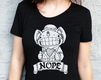 May include: Black t-shirt with a white graphic of a cartoon creature wearing a hat and a bow tie. The creature has large teeth and is holding up two thumbs. The text "NOPE" is written on a banner below the creature.