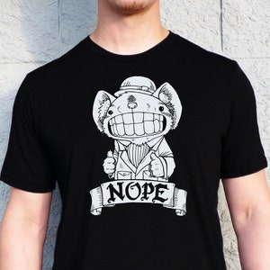 May include: Black t-shirt featuring a white graphic of a cartoon creature wearing a hat and a banner that says "NOPE".