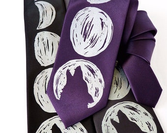 May include: Two silk neckties with a moon and wolf design. One tie is black with silver moons and a wolf silhouette. The other tie is purple with silver moons and a wolf silhouette.