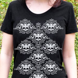 May include: Black t-shirt with a white design of stylized skulls with horns and floral accents.