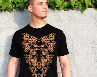 May include: A black t-shirt with a brown butterfly design. The butterflies are arranged in a symmetrical pattern on the front of the shirt.