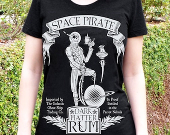 May include: Black t-shirt with a white graphic of a skeleton pirate holding a bottle of rum. The text "SPACE PIRATE" is above the skeleton and "DARK MATTER RUM" is below. The text "Imported by The Galactic Ghost Ship Trading Co." and "80 Proof Bottled in the Parrot Nebula" are on either side of the rum bottle.
