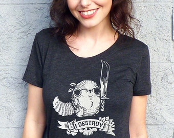 May include: A dark gray t-shirt with a graphic of a cute, cartoon creature holding a knife. The creature is wearing a hat and has a large, round head. The text "I DESTROY" is printed on a banner below the creature.