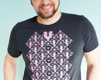 May include: A dark gray t-shirt with a pink and black geometric pattern featuring a heart and a stylized unicorn design.