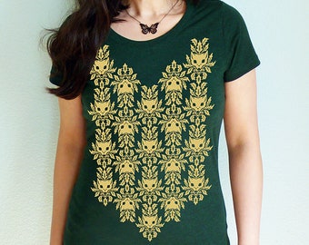 May include: A dark green t-shirt with a gold pattern of stylized cat faces and leaves. The pattern is centered on the front of the shirt and extends from the neckline to the bottom hem.