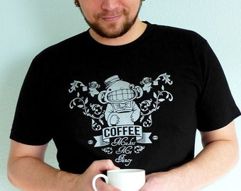 May include: A black t-shirt with a white graphic design of a cartoon monkey holding a coffee cup. The text on the shirt reads "Coffee Makes Me Zing".