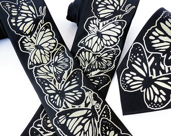 May include: Two black silk ties with a white butterfly pattern. The ties are made of a smooth, silky fabric and have a classic design.
