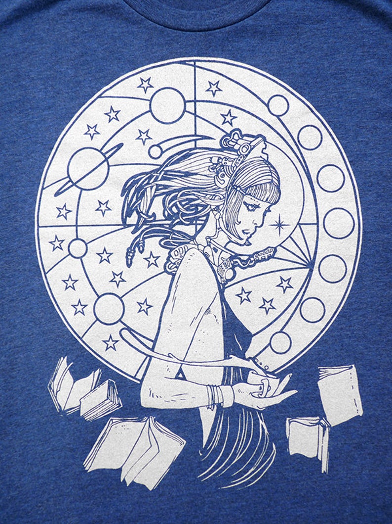 May include: A white graphic design on a blue t-shirt features a woman with long hair standing inside a circle with stars and planets. The woman is holding books in her hands.